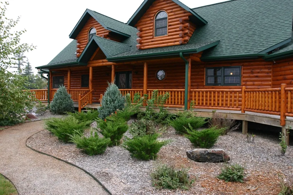 Log home with a gravel landscape bed, evergreen shrubs, and a curved border