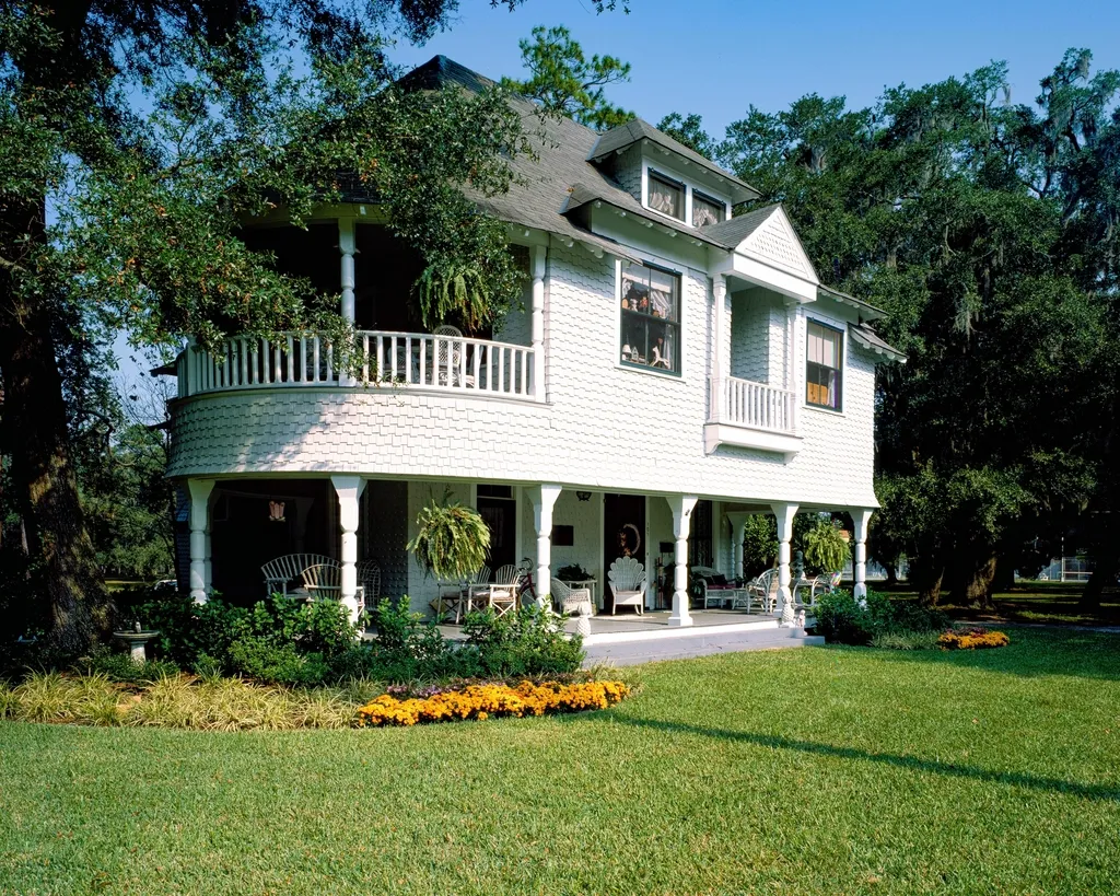 White home with a wraparound porch, flower borders, and a manicured lawn