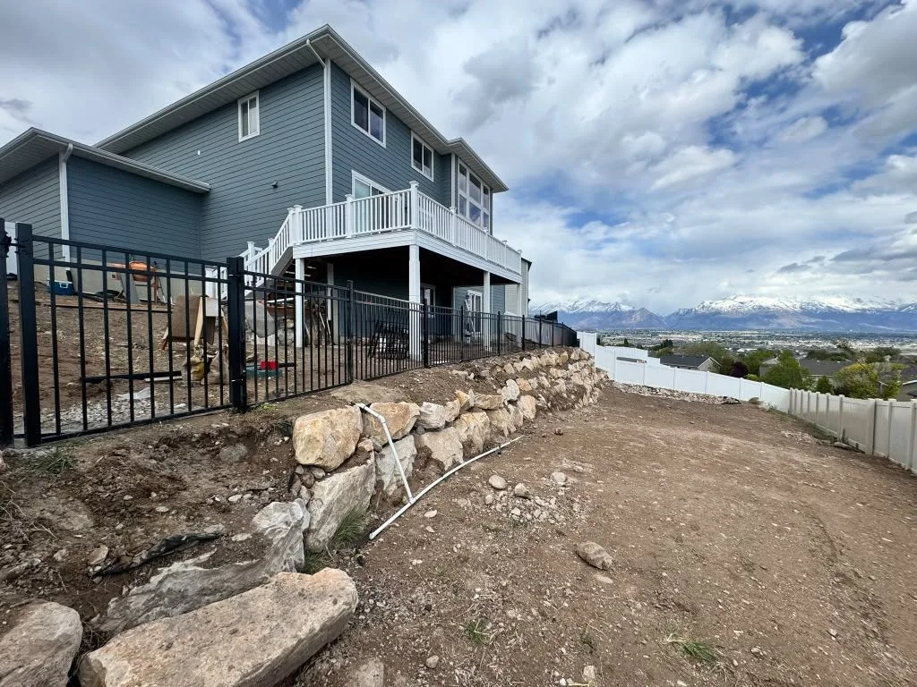 Black aluminum fence above a boulder retaining wall, with a white vinyl fence and mountain views