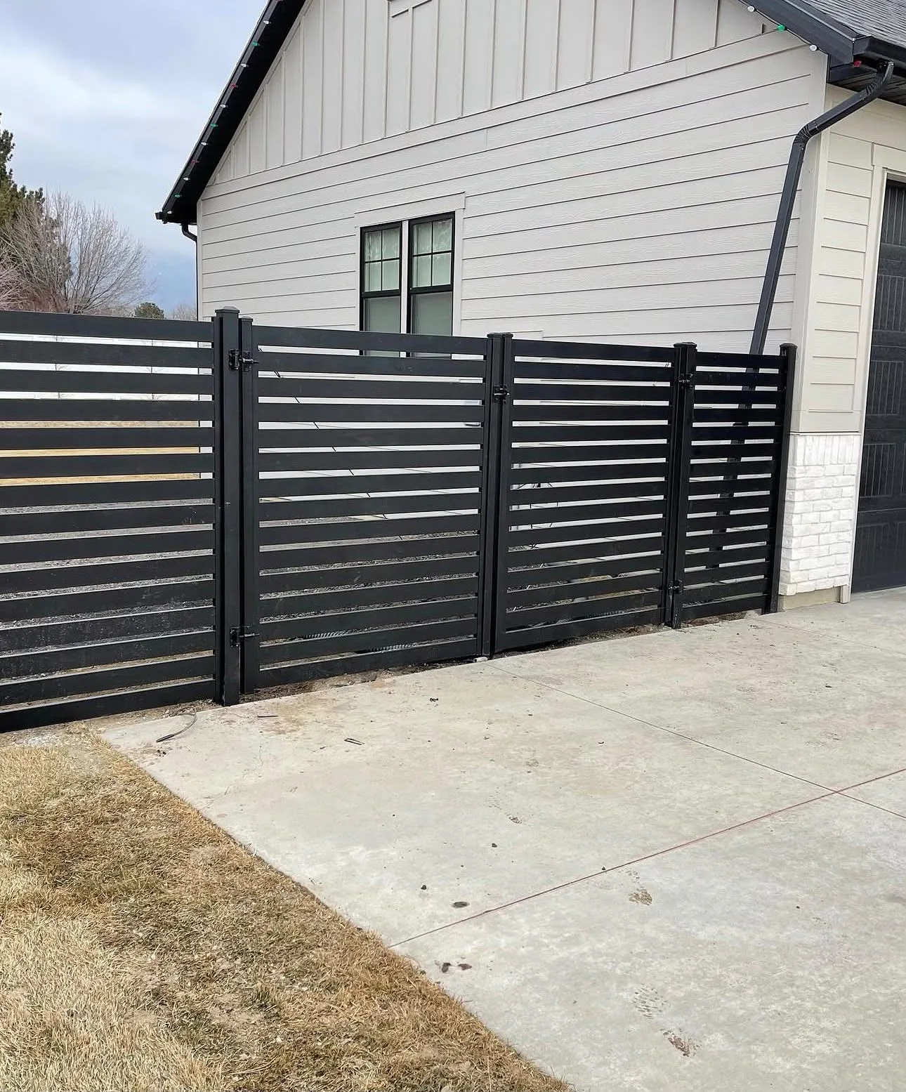 Black horizontal slat privacy fence and gates beside a driveway