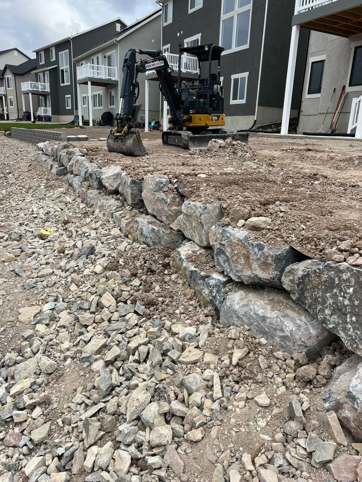 Mini excavadora nivelando un patio junto a un muro de contención de rocas nuevo