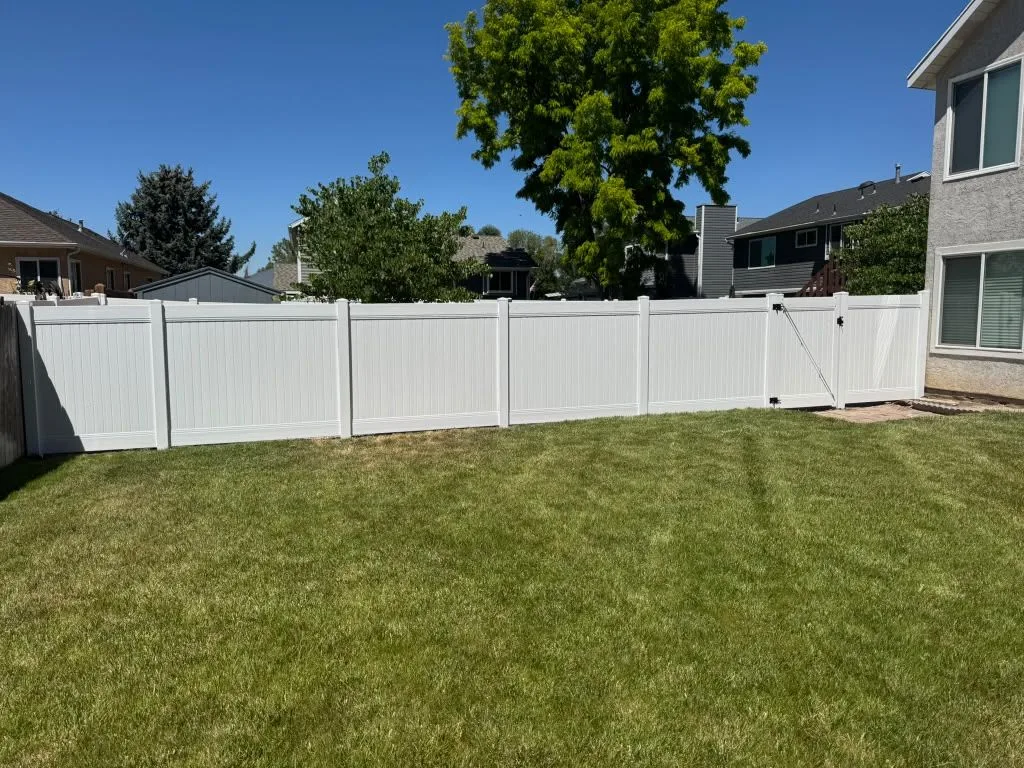 White vinyl privacy fence with a gate around a green backyard lawn