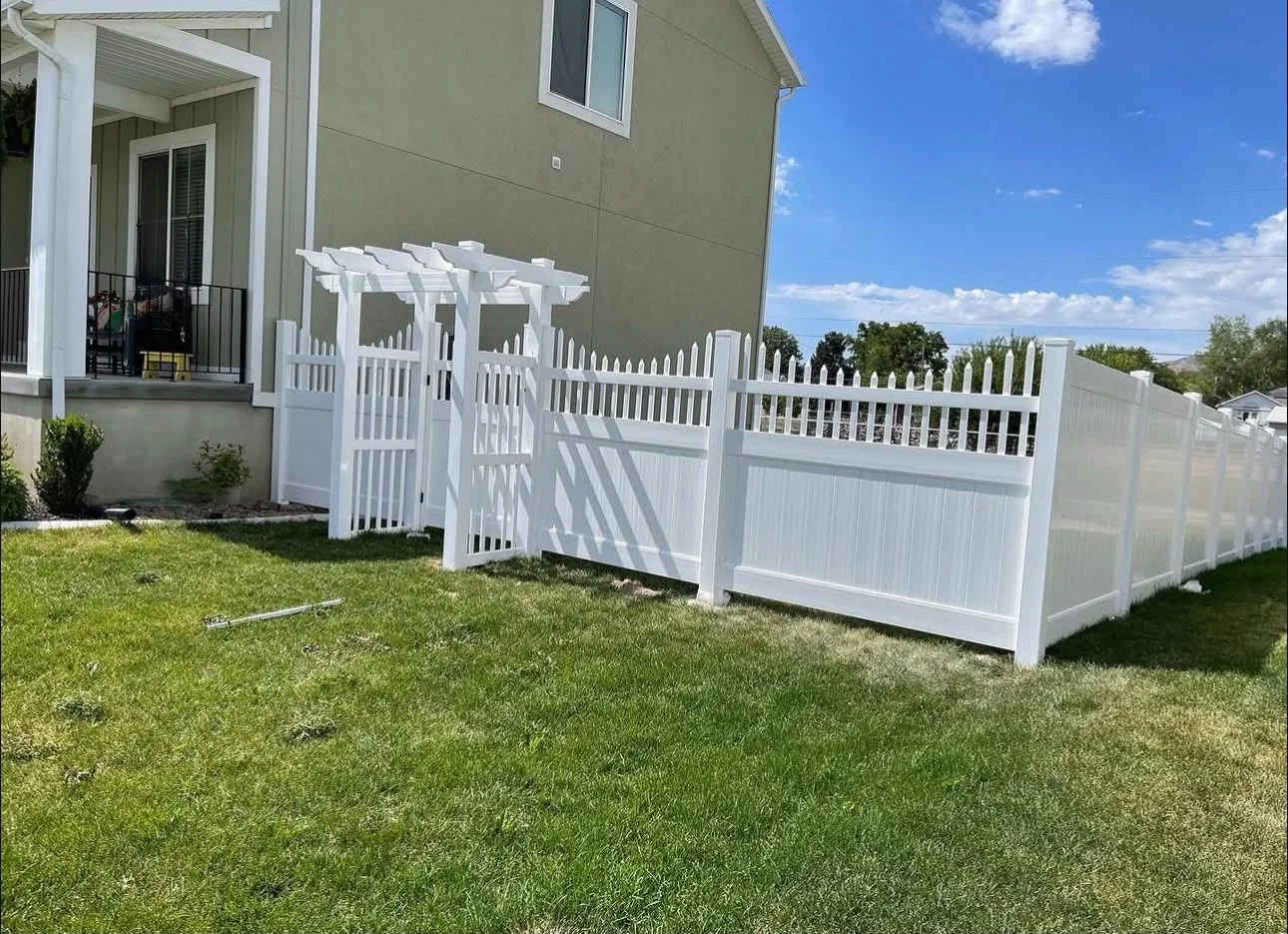 Cerca de vinil blanco con portón de pérgola, paneles con remate de piquetes y tramo de privacidad junto al pasto