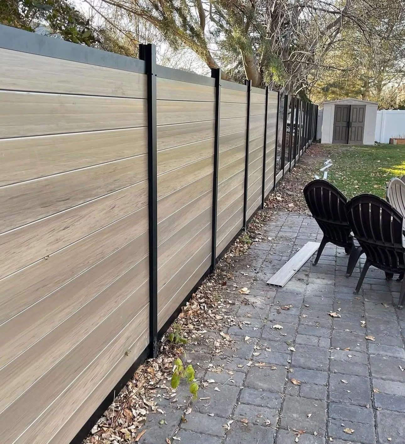 Horizontal woodgrain privacy fence with black posts along a stone patio
